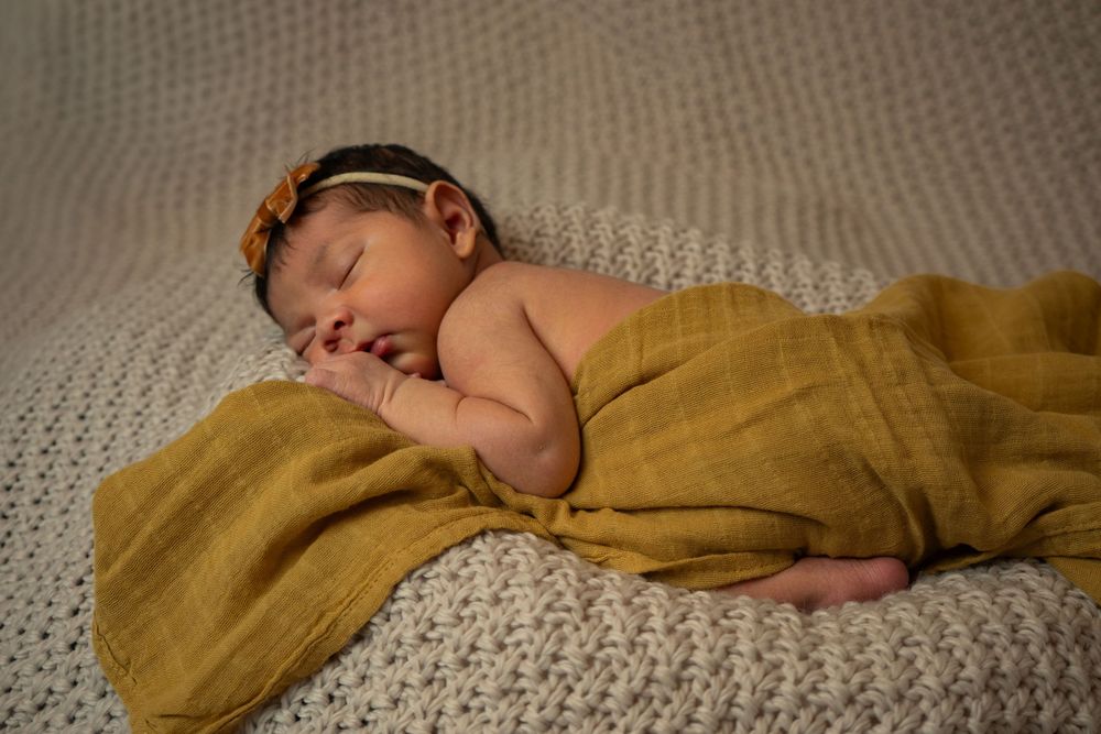 Sleeping baby draped in soft mustard fabric on textured carpet.