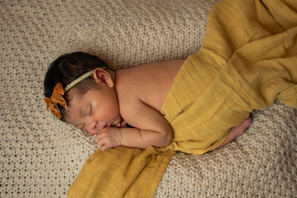 Peaceful newborn resting on cream carpet with golden yellow wrap.