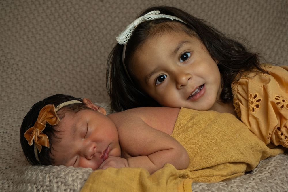 Sweet moments captured of baby with yellow fabric on textured rug.