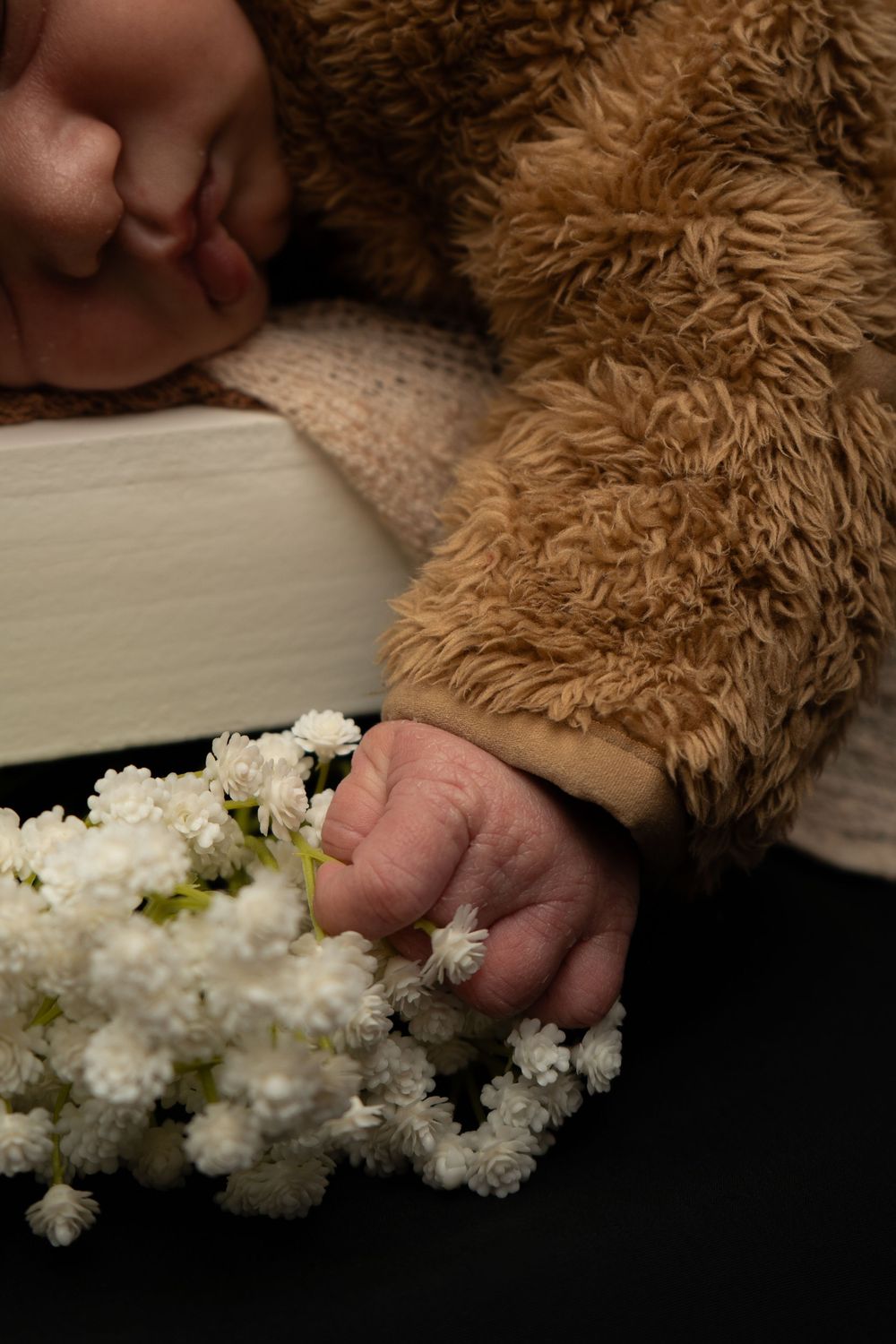A soft brown teddy bear rests near delicate white flowers on a light colored surface.