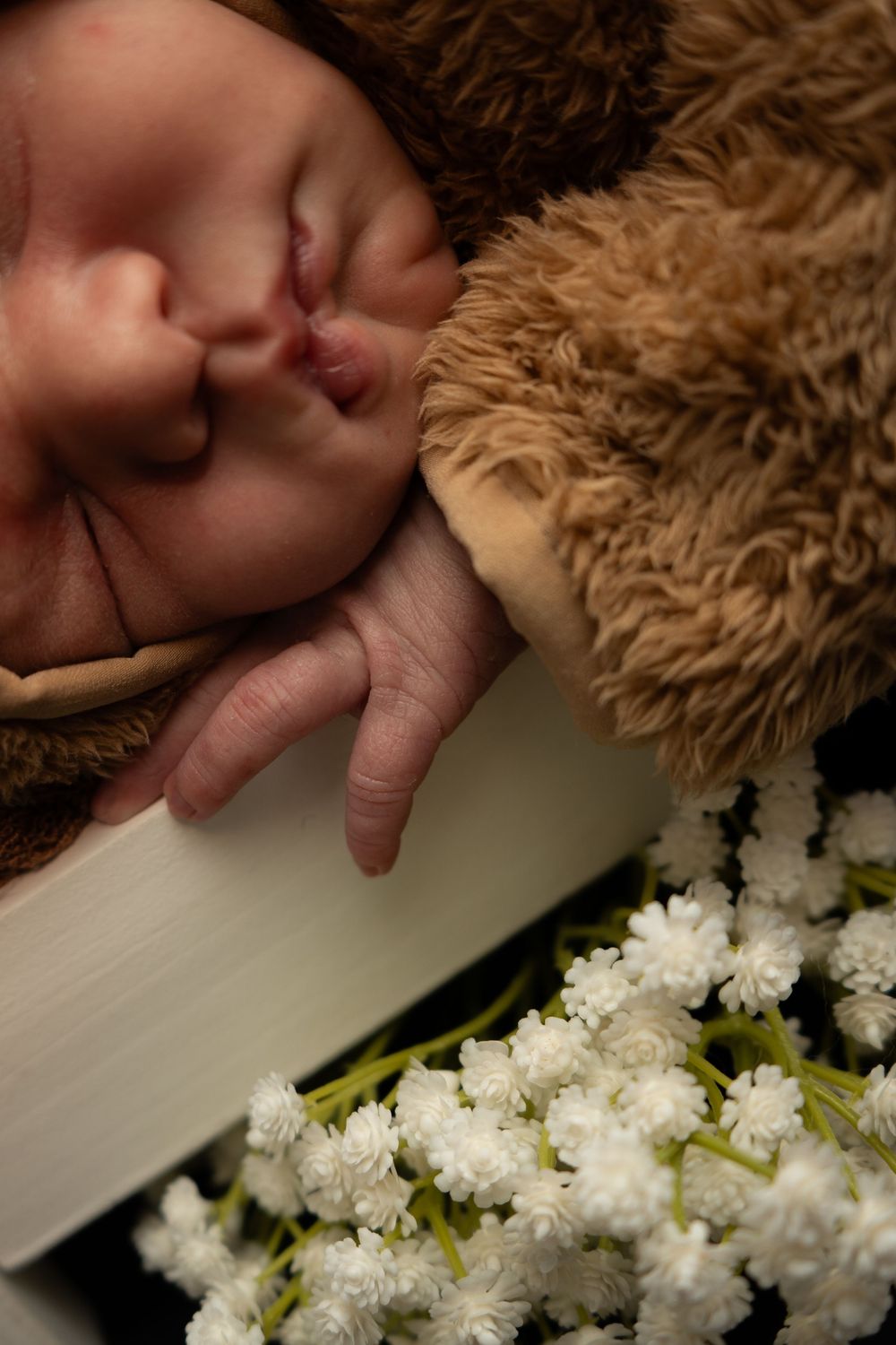 A sleeping baby lies peacefully next to delicate white cherry blossoms arranged in a row.