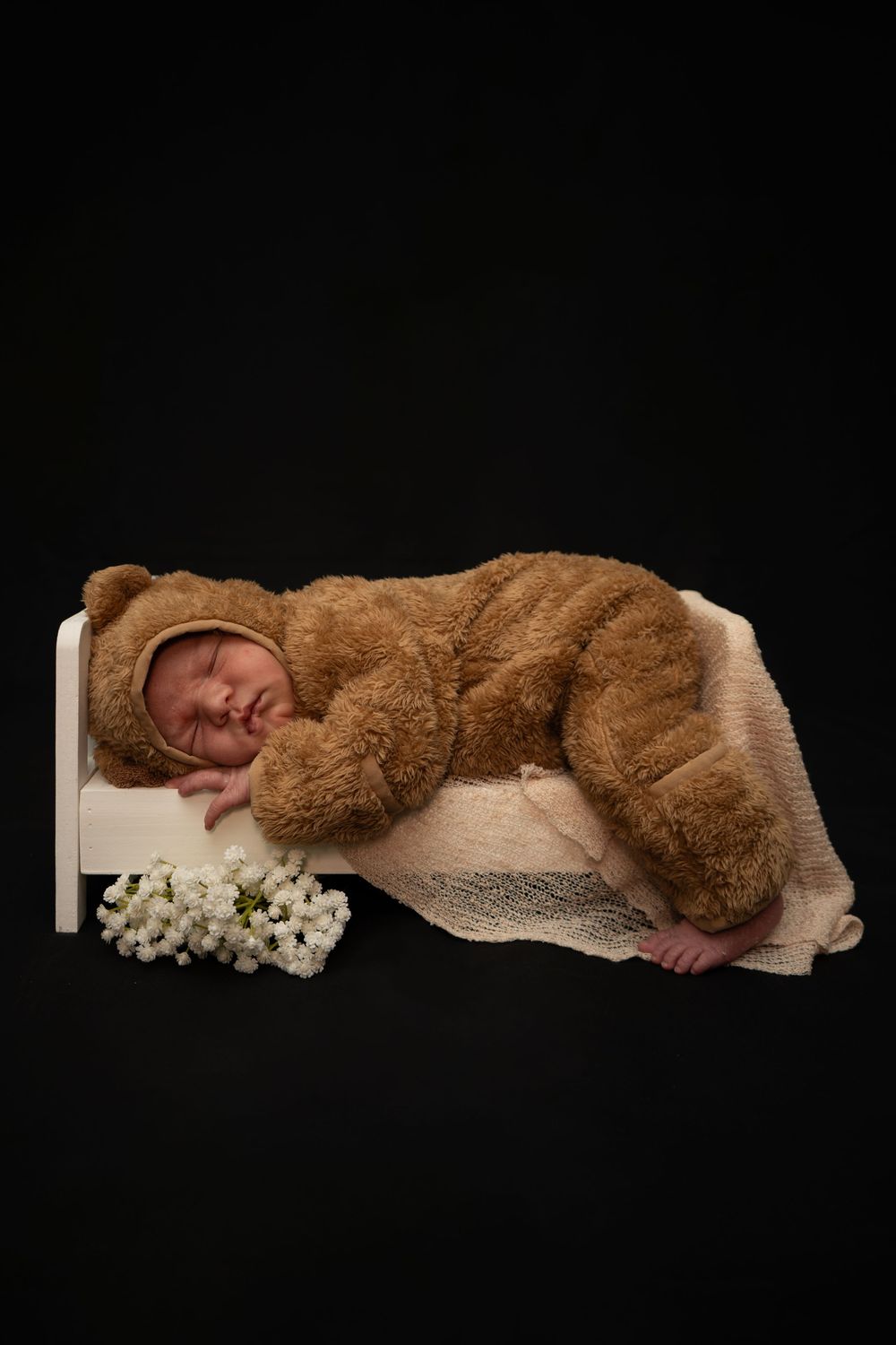 A baby rests peacefully on a brown fluffy blanket against a black background in a studio setting.
