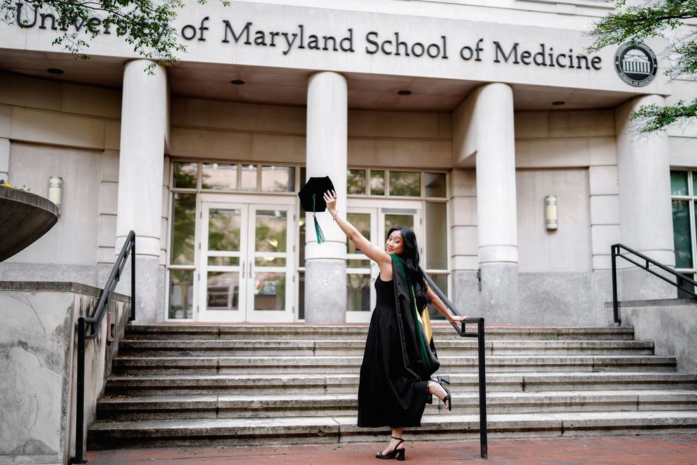 Graduate celebrates in front of University of Maryland School of Medicine, tossing cap in black gown, in Baltimore, MD, graduation session
