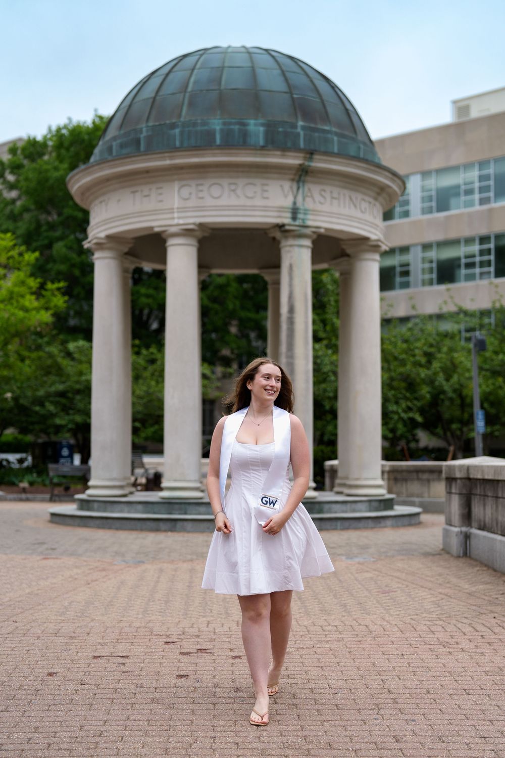 Young woman in white dress smiling near The George Washington University iconic colonnade on campus, graduation session in DC