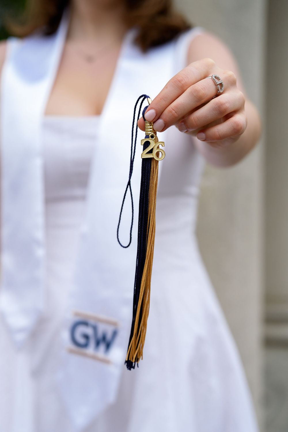 GW graduation tassel held by student in white dress with GW stole, during graduation session in Washington DC