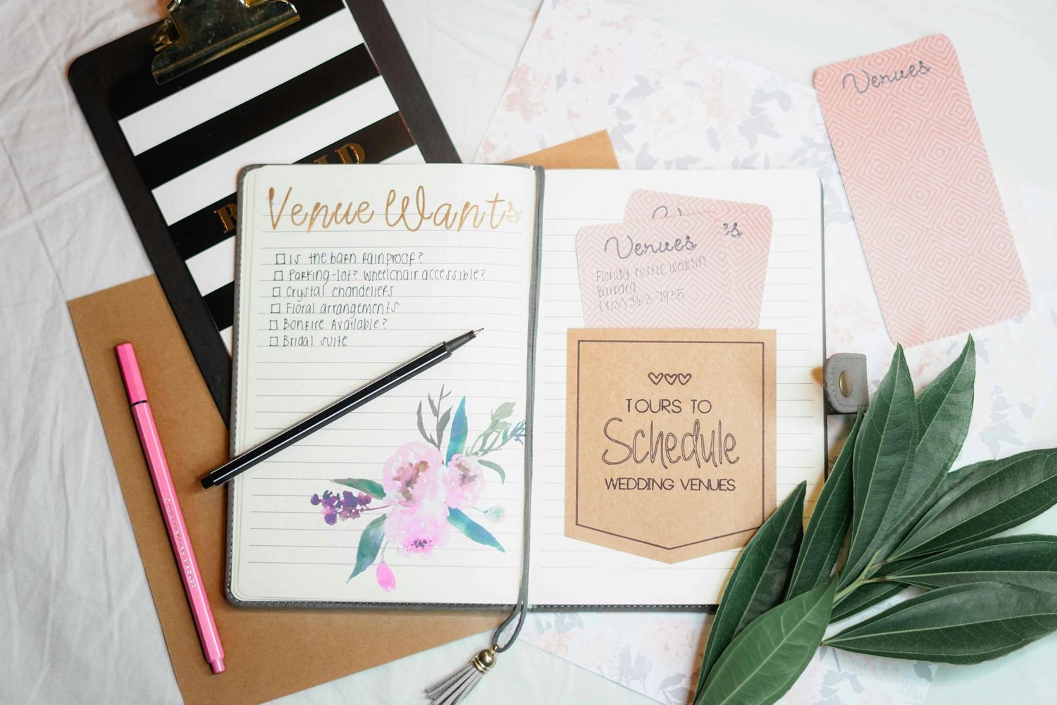 A minimalist desk scene with pink and white flowers in tin can vase, notebooks, phone and single rose on open journal.