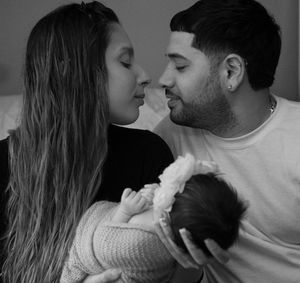 A loving couple shares an intimate moment while holding their newborn baby in a tender black and white portrait.