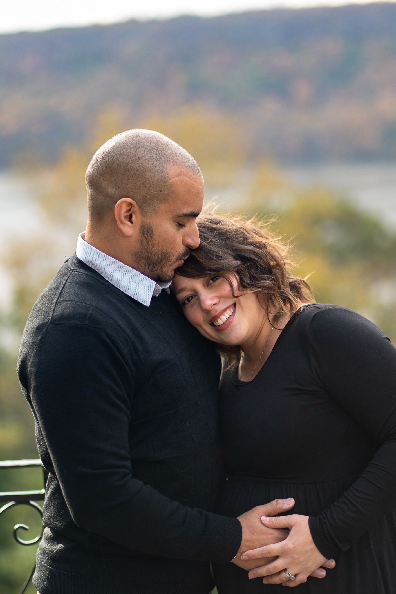 Intimate maternity portrait of couple embracing outdoors with natural autumn scenery in background.