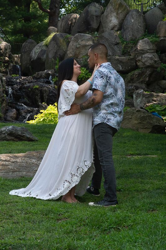 Romantic couple in wedding attire sharing tender moment by rock garden waterfall.