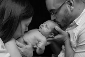 Parents sharing tender moment with their newborn baby in intimate black and white portrait.