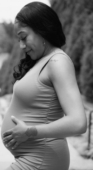 Side view black and white portrait of pregnant woman touching belly with gentle expression.
