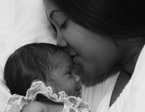 A black and white intimate portrait of a loving moment between a mother and baby in lace clothing.