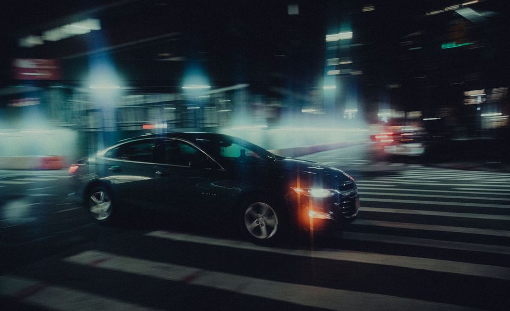 Car driving through a rainy city intersection at night with blurred lights creating a moody atmosphere.