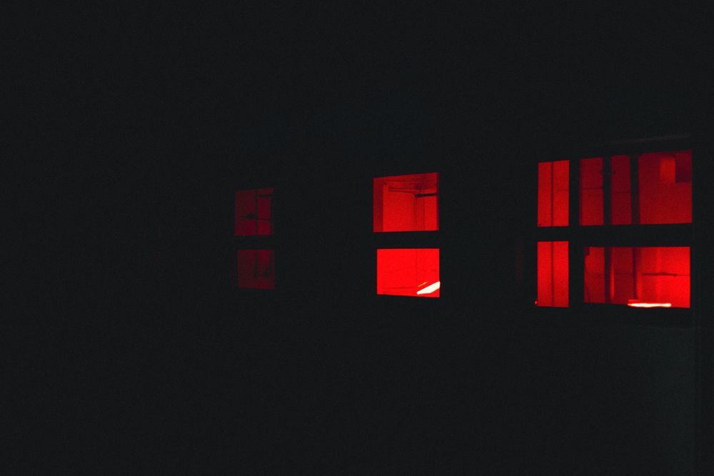 Three windows glowing with red light against a dark building exterior at night.