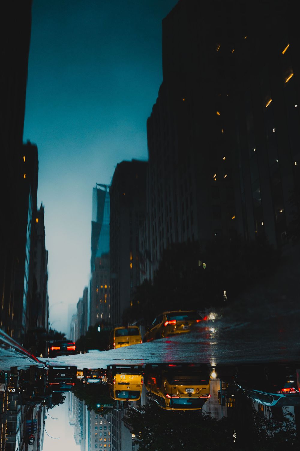 Wet city street reflects neon lights and skyscrapers during blue hour.