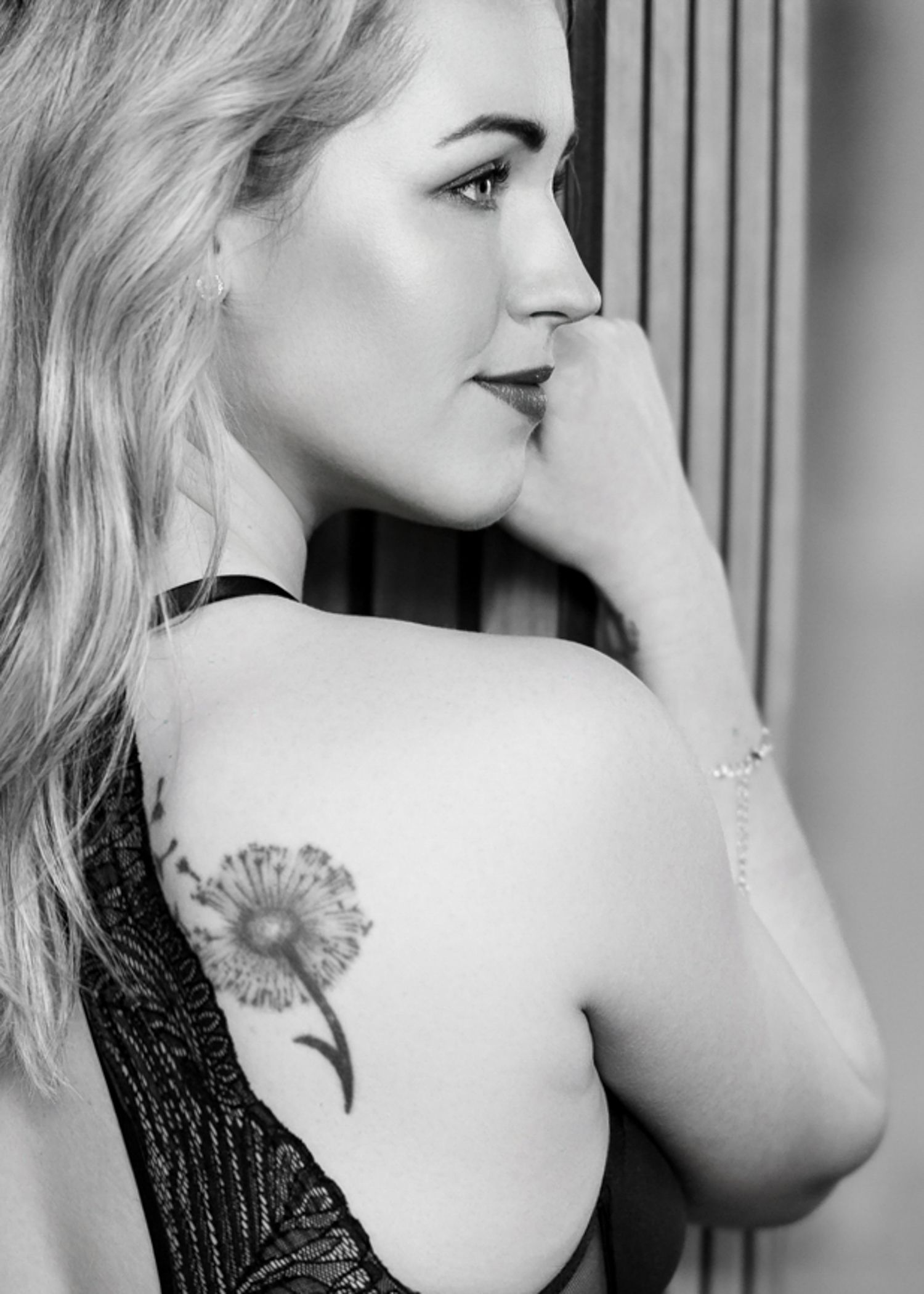 Black and white portrait showing dandelion tattoo on woman's bare shoulder.