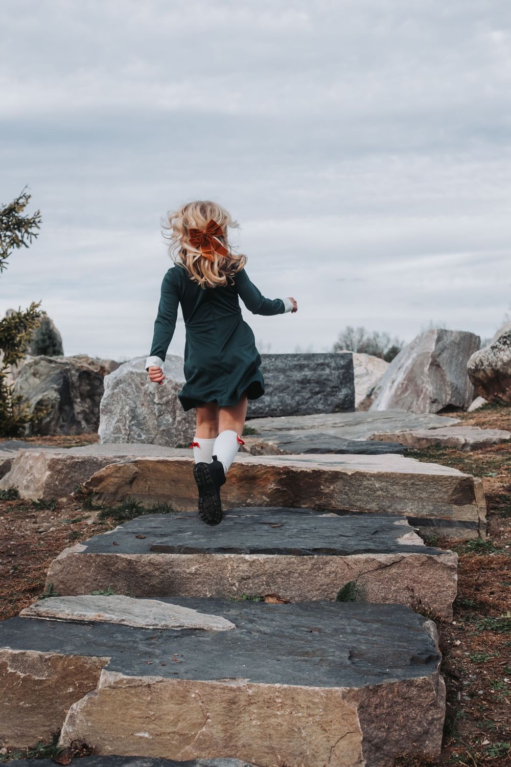 A young girl skips away from the camera. She has a red bow in her curly blonde hair.