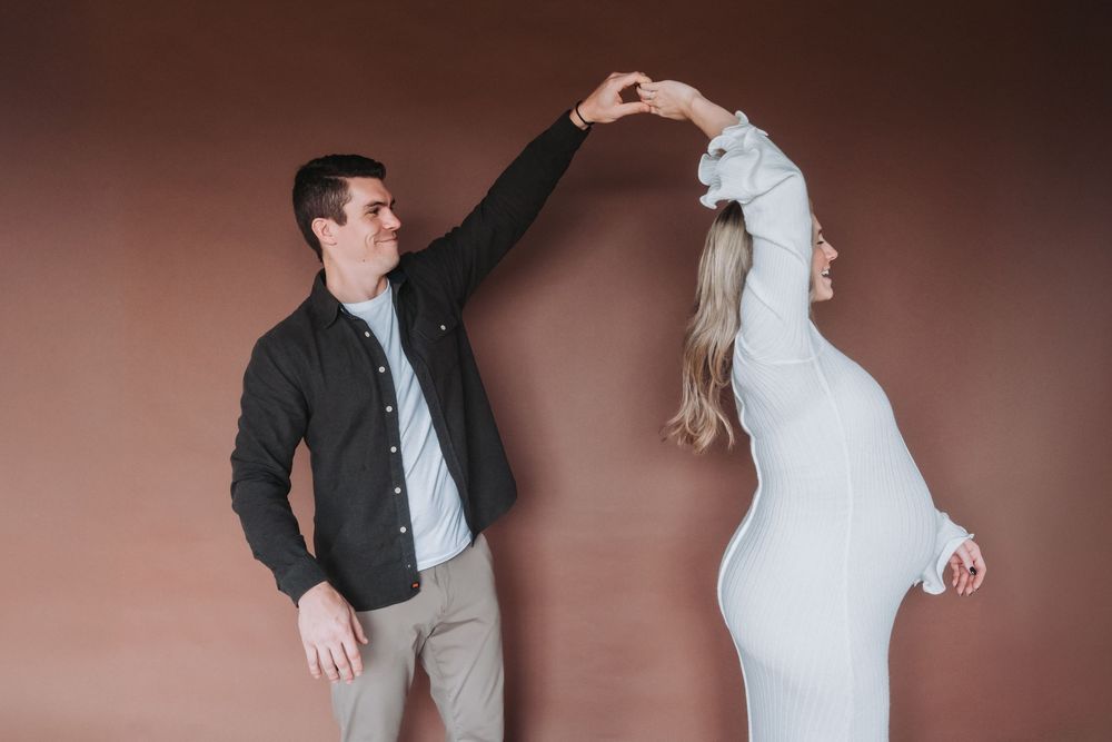 A couple dances together. The wife is pregnant and wears a white dress.