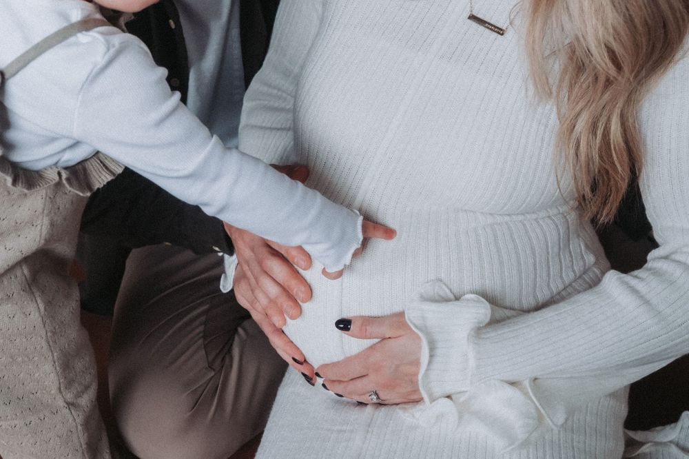 A toddler points at her mother’s pregnant belly.
