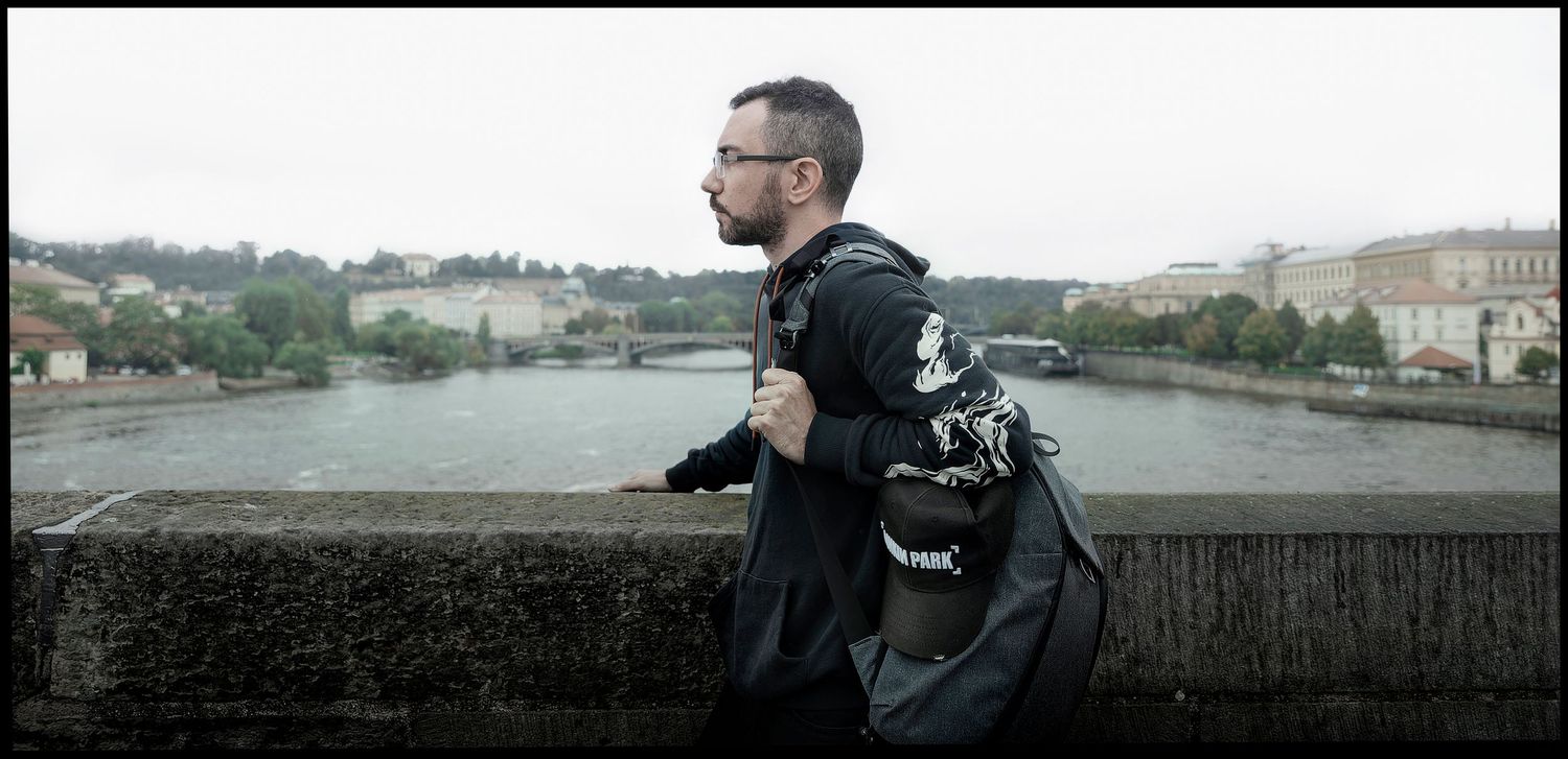 Runner in black athletic wear jogging along a stone wall with a city backdrop and cloudy sky.