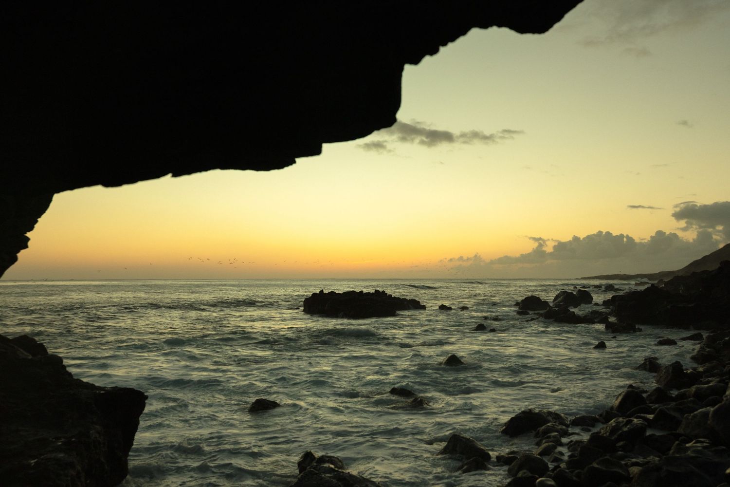 Two figures in flowing white clothing walk along a scenic coastal cliff with mountains and ocean in the background at sunset.