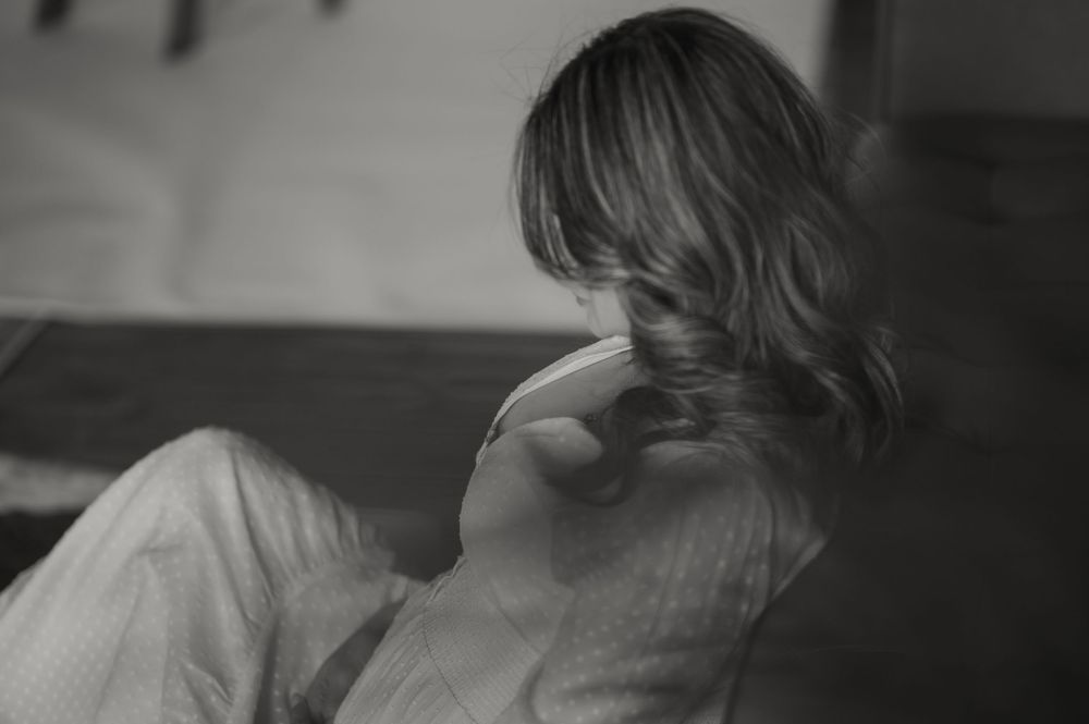 A grainy black and white artistic photograph showing a figure in soft focus turned away from the camera.