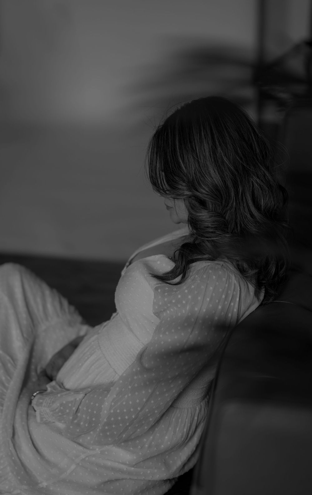 A black and white artistic silhouette photo showing a woman in a flowing dress sitting near a window.