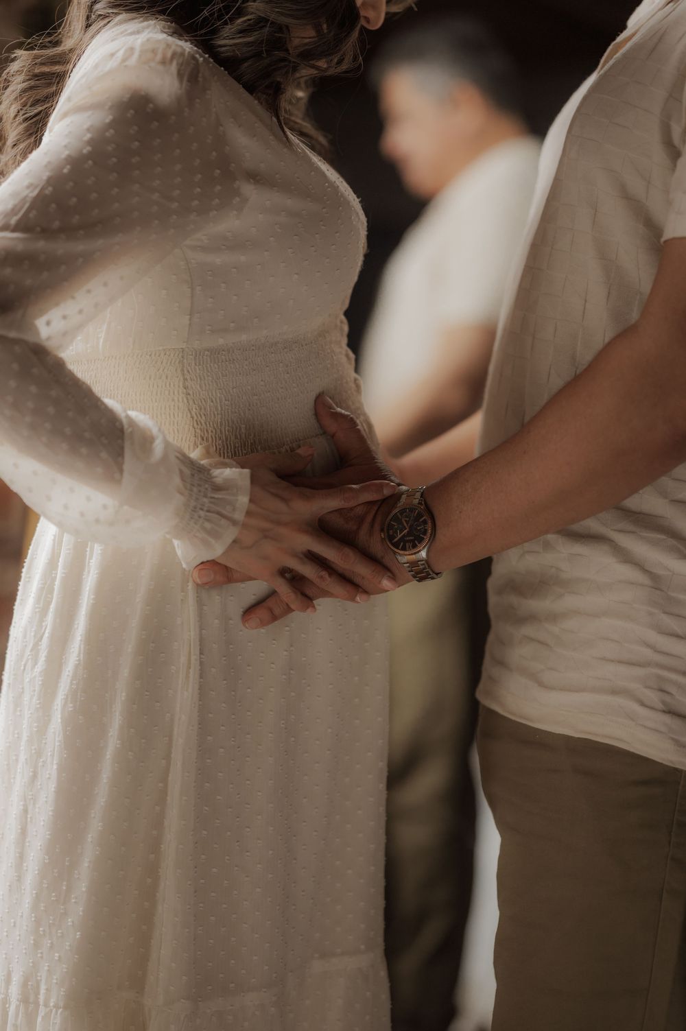 Close-up of couple in white dress and casual wear holding hands together in intimate moment.