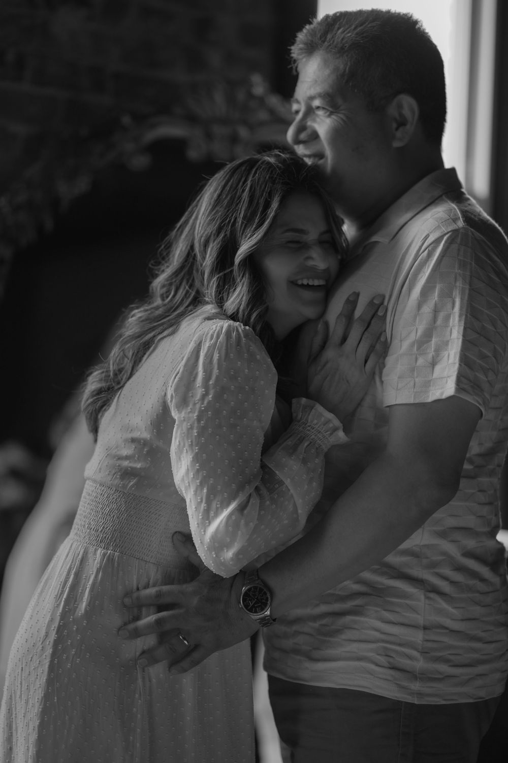 A couple shares an intimate embrace while laughing together in a black and white romantic portrait.