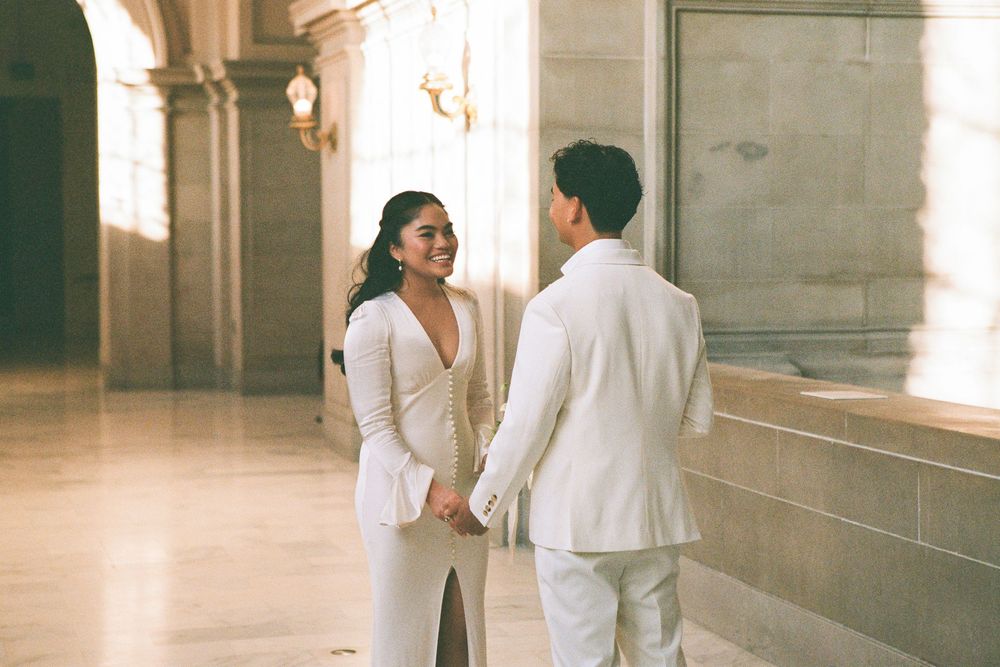 A couple in white outfits shares an intimate moment in an elegant hallway with natural light.