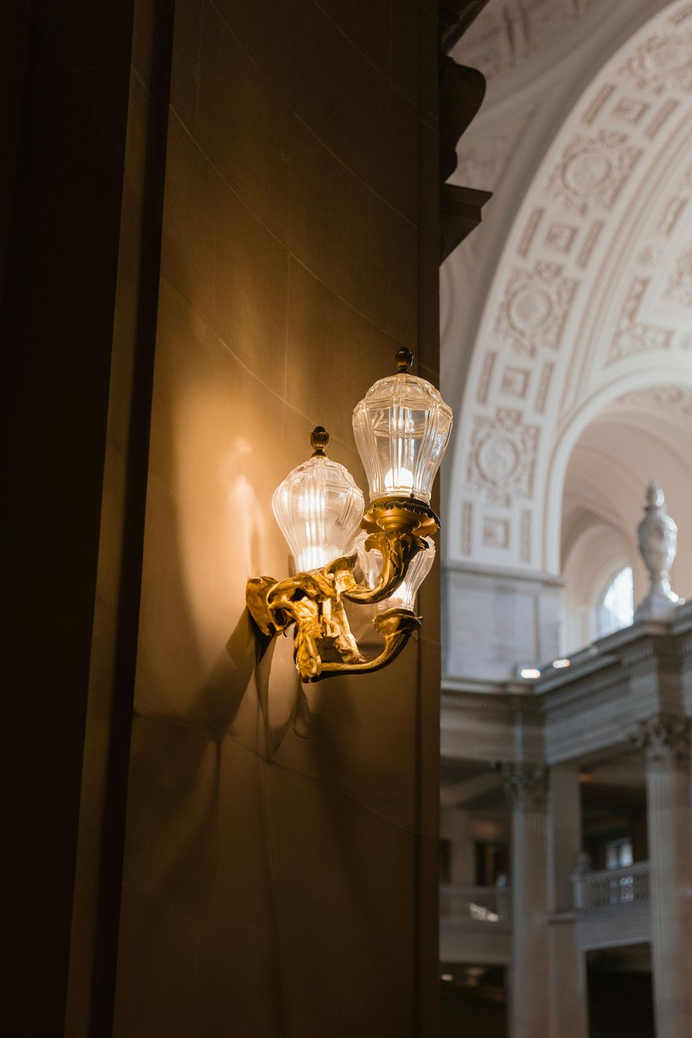 An ornate vintage wall sconce illuminates an architectural detail in warm light.
