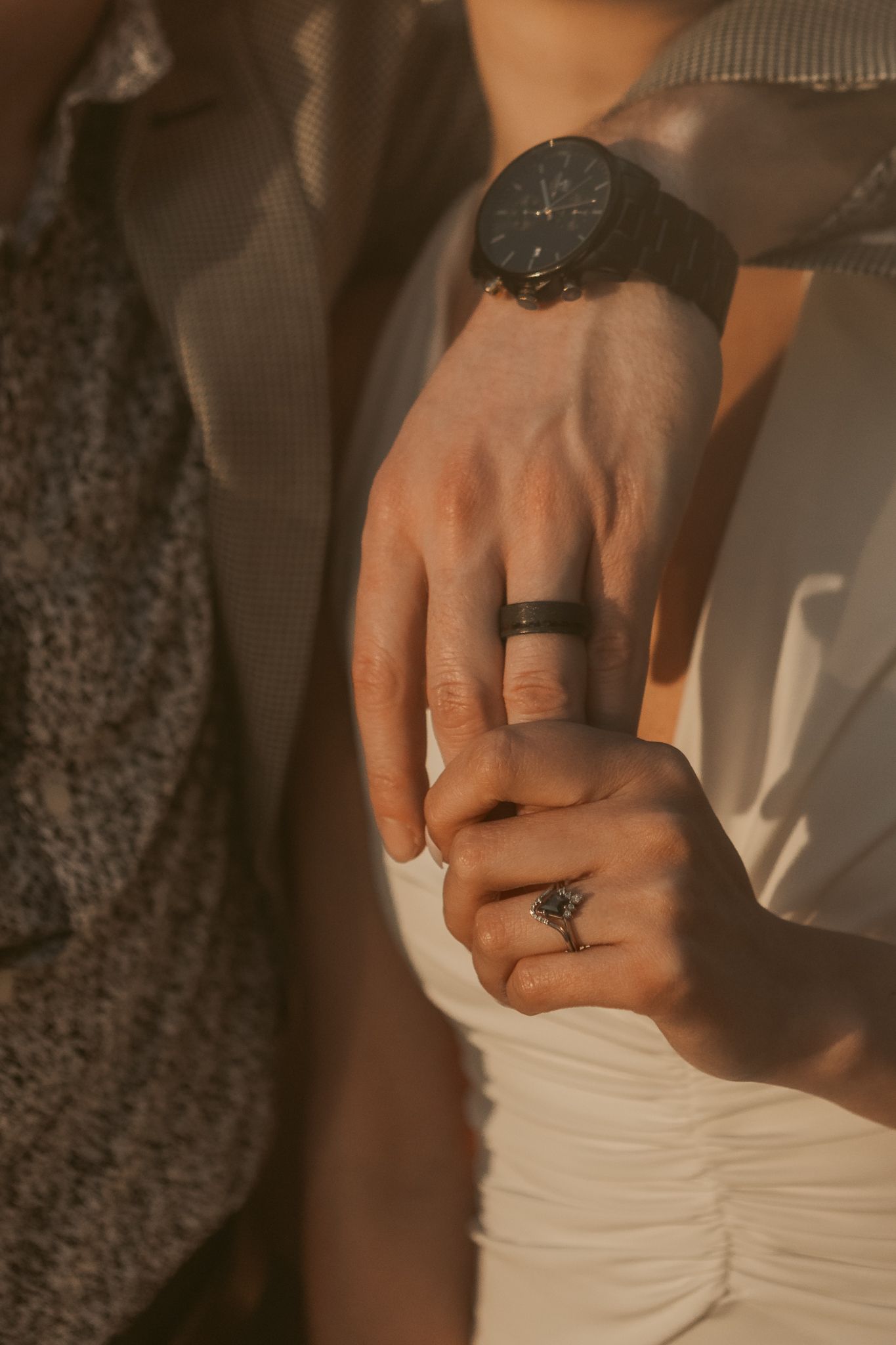 Close-up of hands of a man placing engagement ring on woman's finger during golden hour.