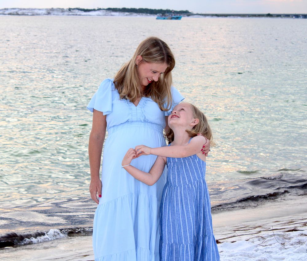 A parent and child in blue dresses share a joyful moment together at sunset on a beach.