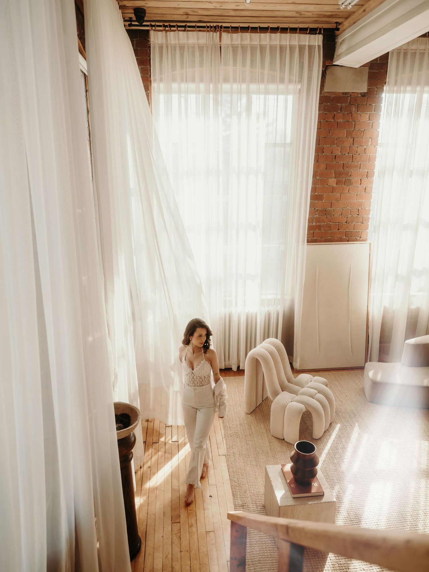 Sunlit room with flowing white curtains, hardwood floors and exposed brick walls creates a dreamy atmosphere.