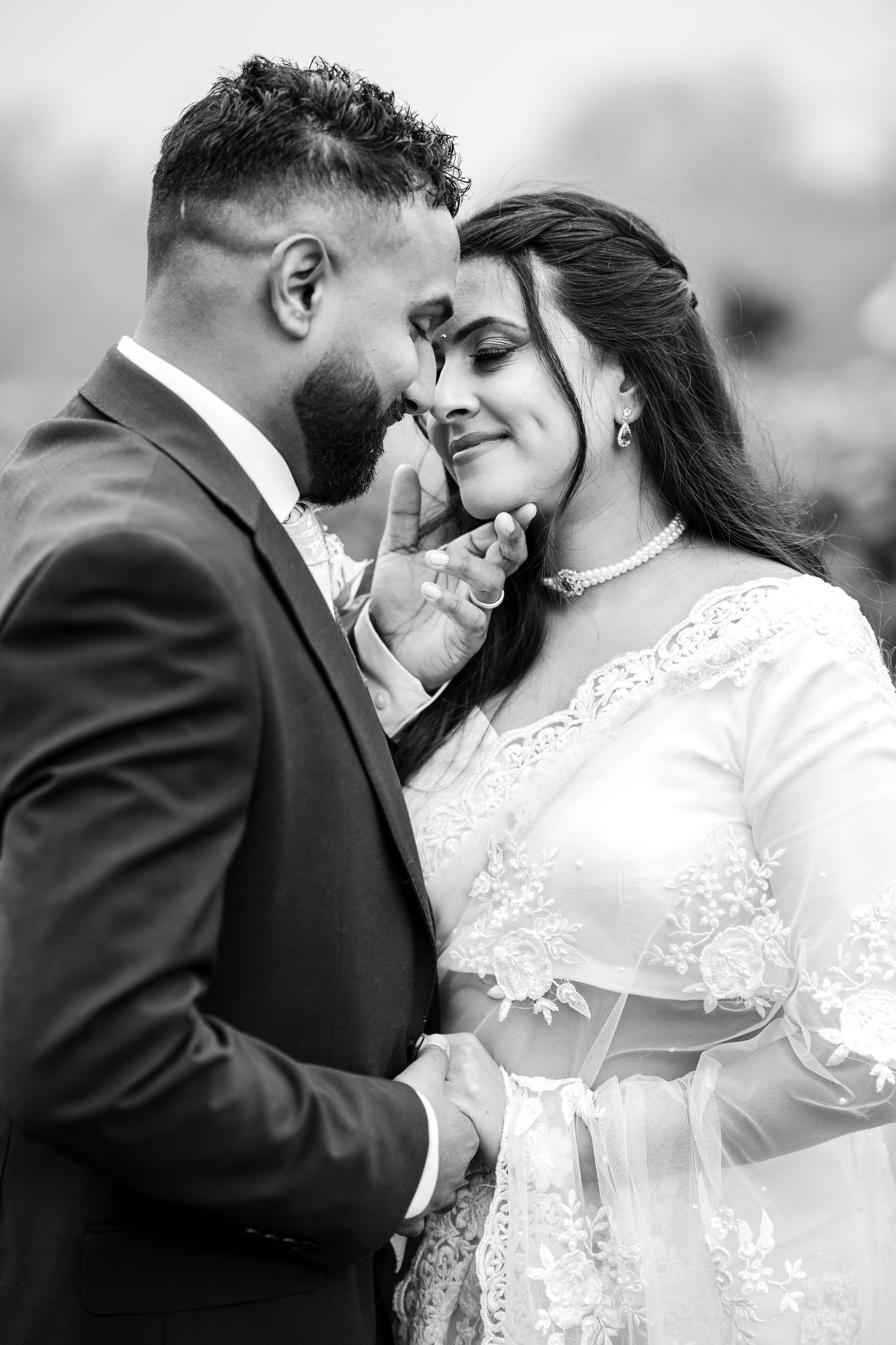A loving black and white wedding portrait shows an intimate moment between newlyweds in formal attire.