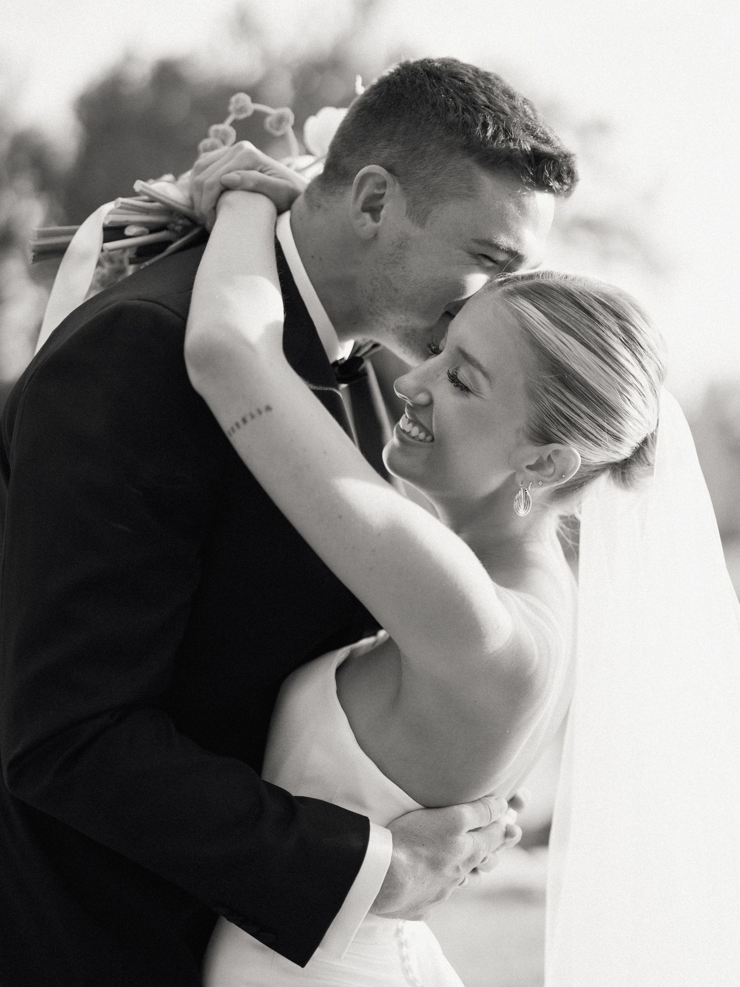 Black and white silhouette of a couple exchanging vows during a wedding ceremony by large windows with floral arrangements.