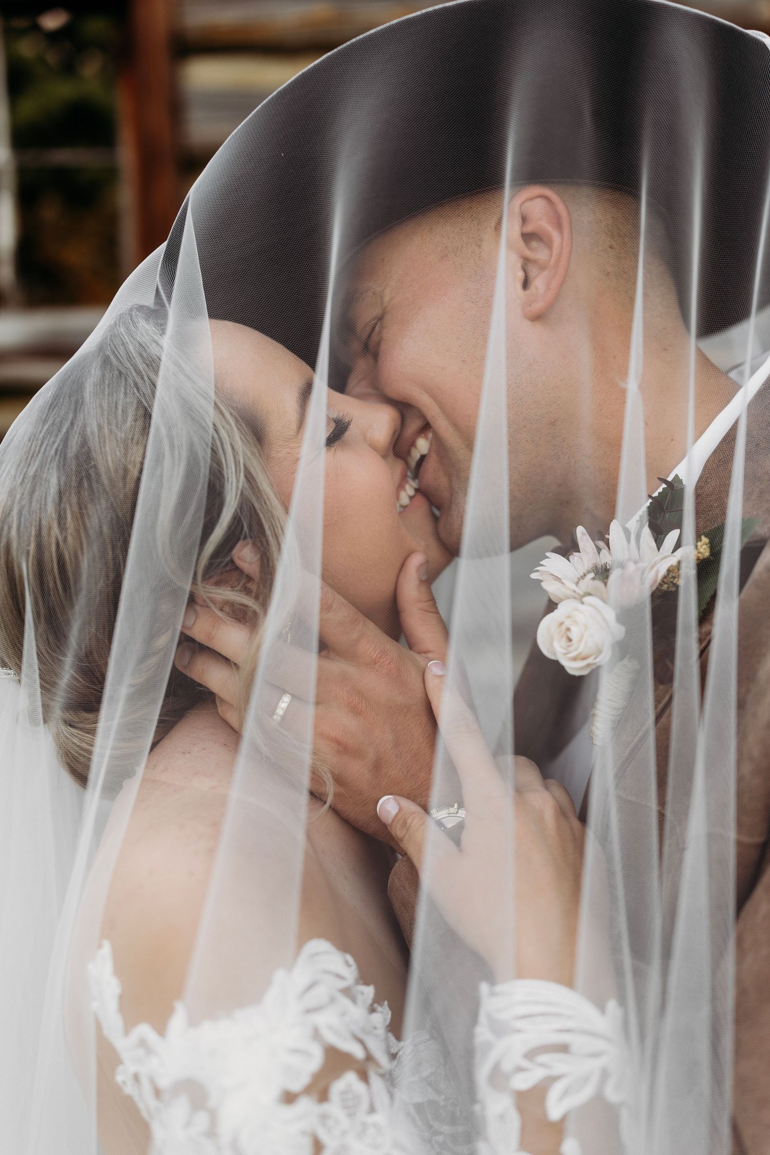 Bride and groom sharing a romantic kiss beneath a flowing white wedding veil.