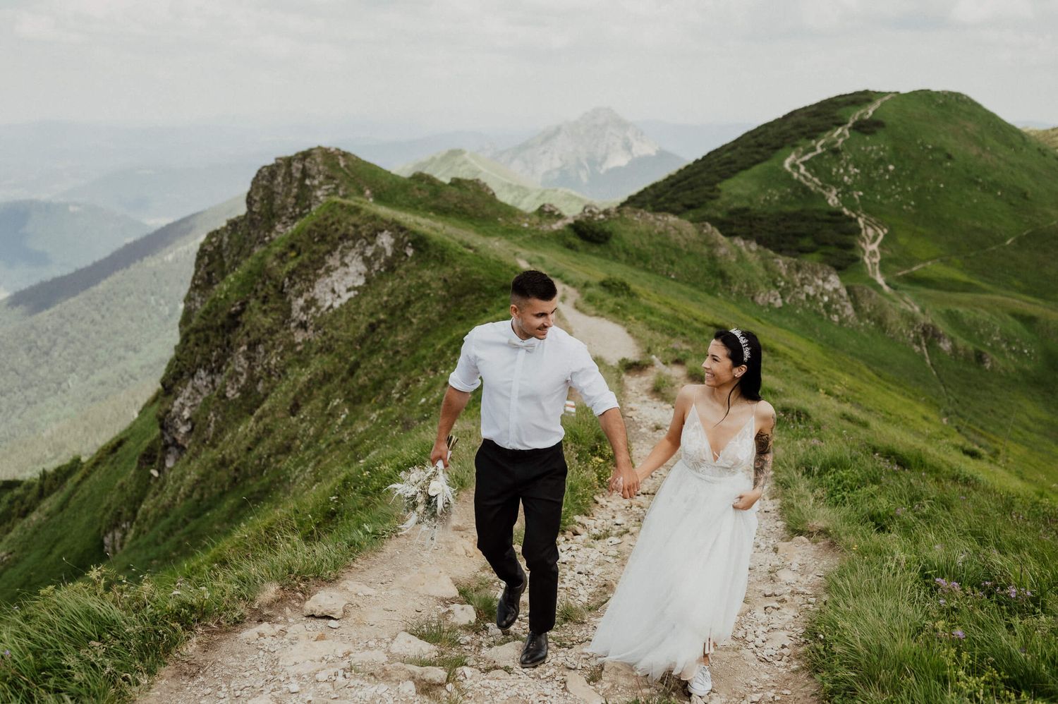 Couple runs joyfully along mountain trail with stunning alpine views.