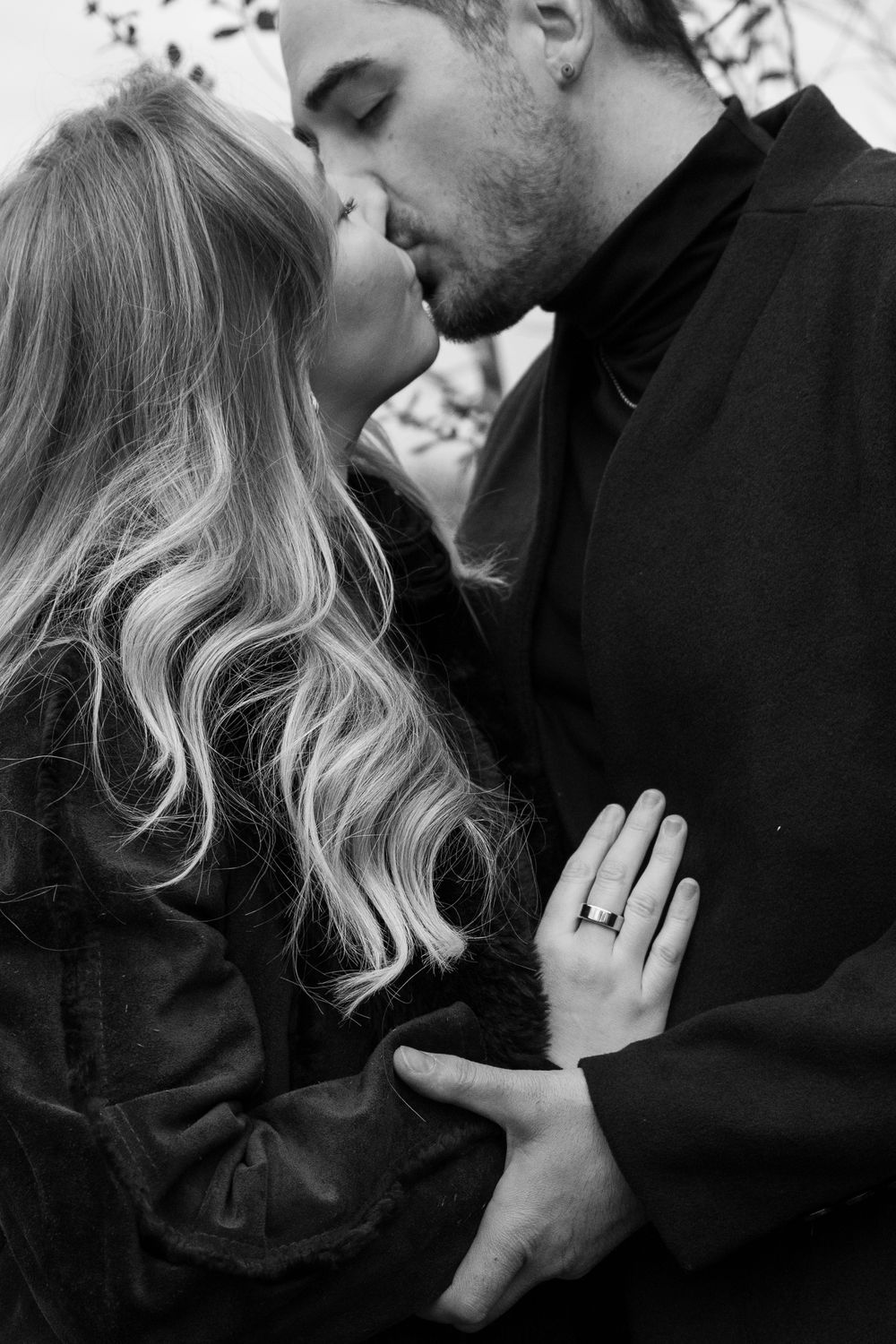 Black and white intimate photo of a romantic couple sharing a kiss, with her wavy blonde hair flowing and hand on his chest.