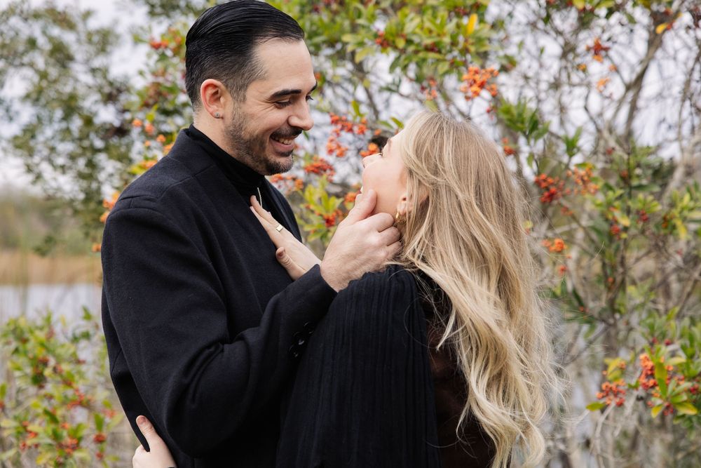 A couple in black winter coats share a romantic moment outdoors during autumn with red berries in the background.