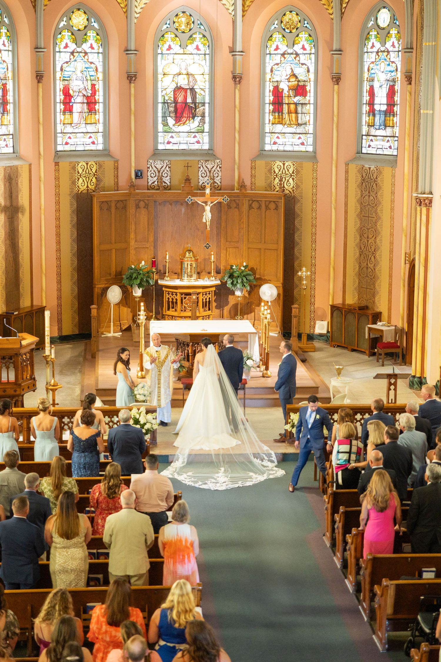 A traditional church wedding ceremony in progress with guests seated in wooden pews and stained glass windows lining the walls. Michigan