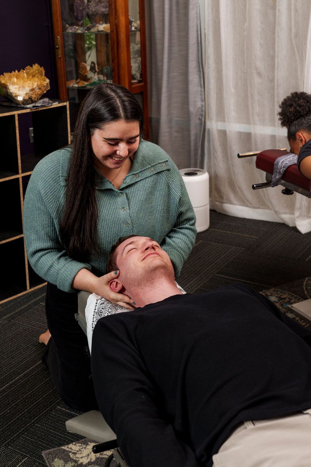 Medical professional performs neck adjustment therapy on a patient lying on treatment table.