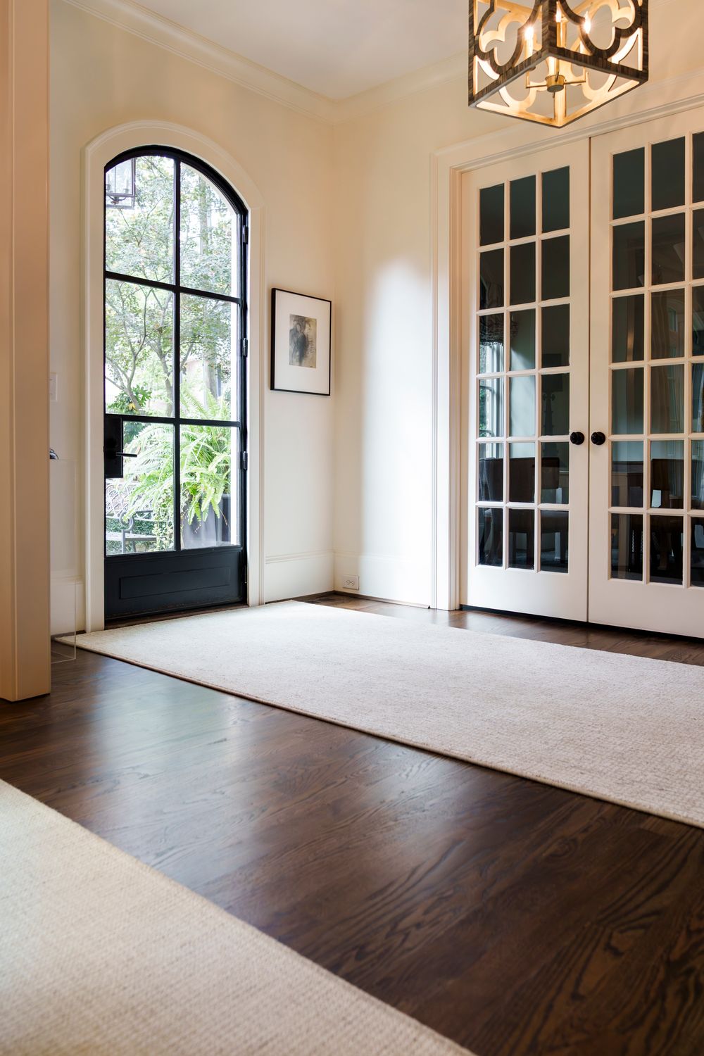 Bright room with arched windows, French doors, and contrasting dark hardwood floors and light carpet.