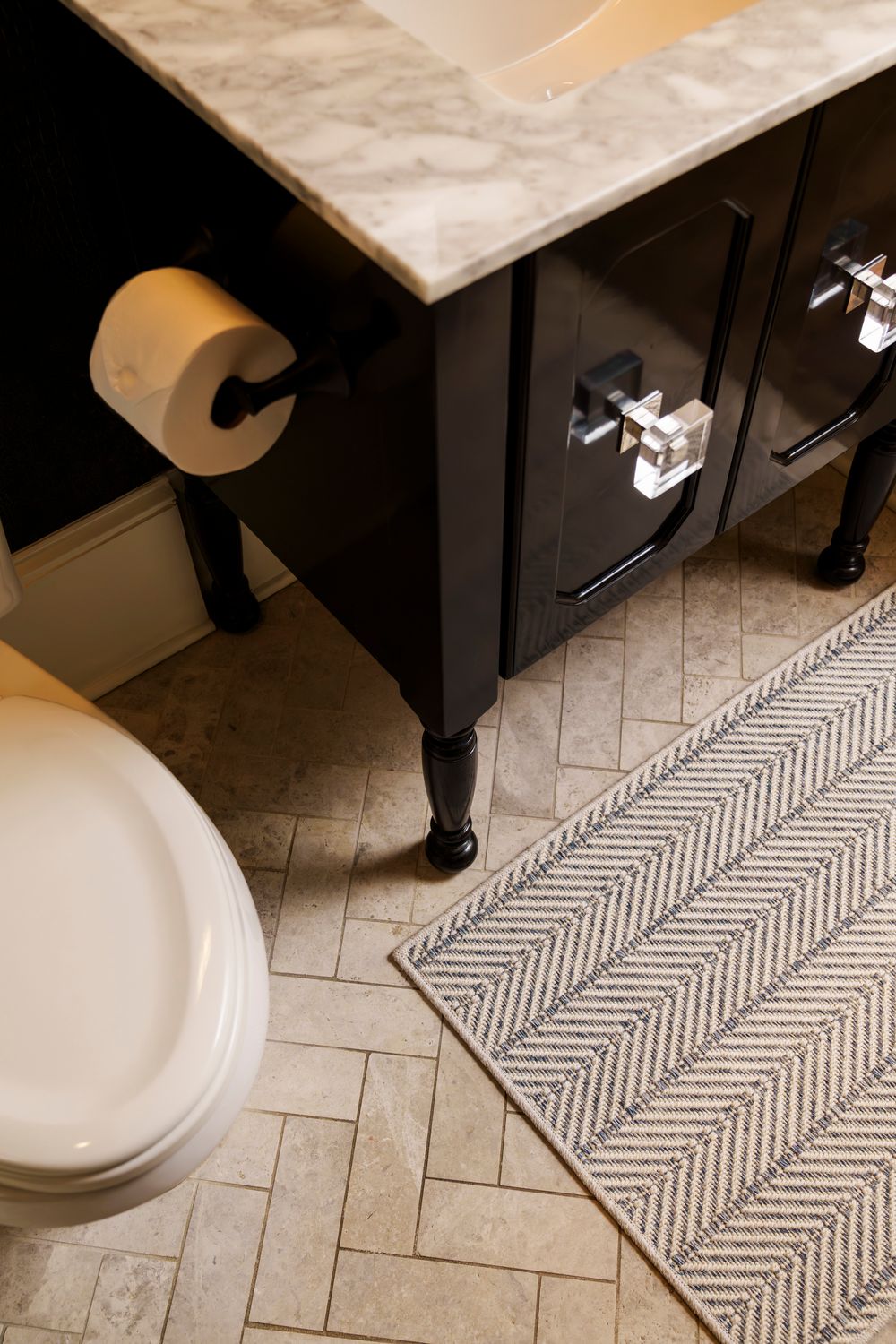 A bathroom floor featuring a geometric patterned runner rug against light tile flooring near a white toilet base.