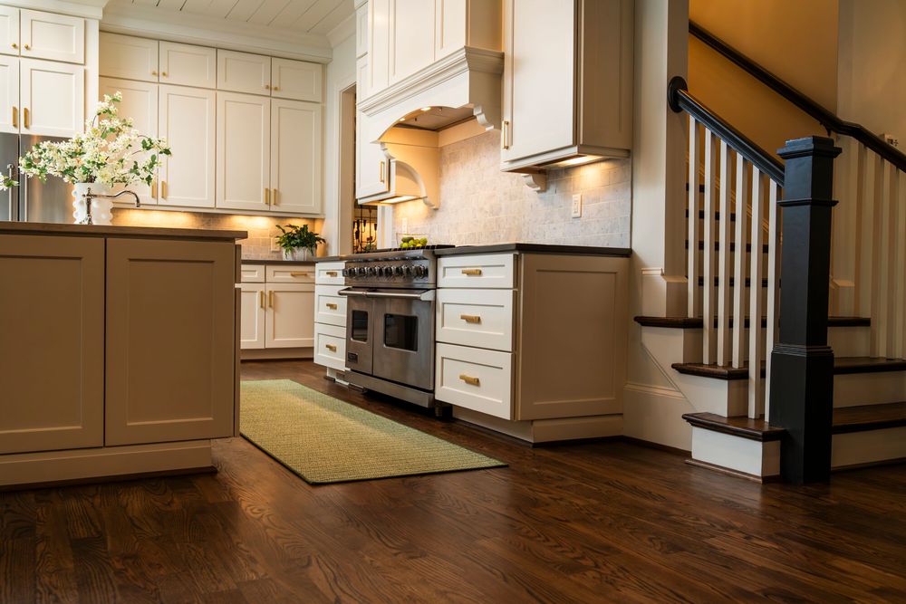 Modern kitchen features white cabinets, dark hardwood floors, and stainless steel appliances with elegant stair railings.