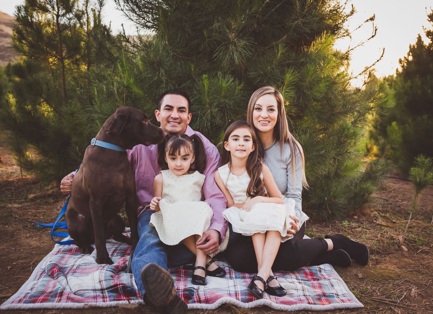 People sitting on a colorful blanket for a family photoshoot in a wooded outdoor setting during golden hour.
