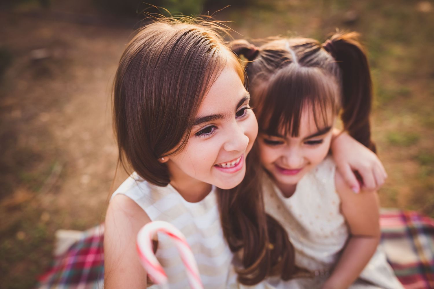 Two friends sharing a joyful moment while sitting on a picnic blanket outdoors in warm lighting.