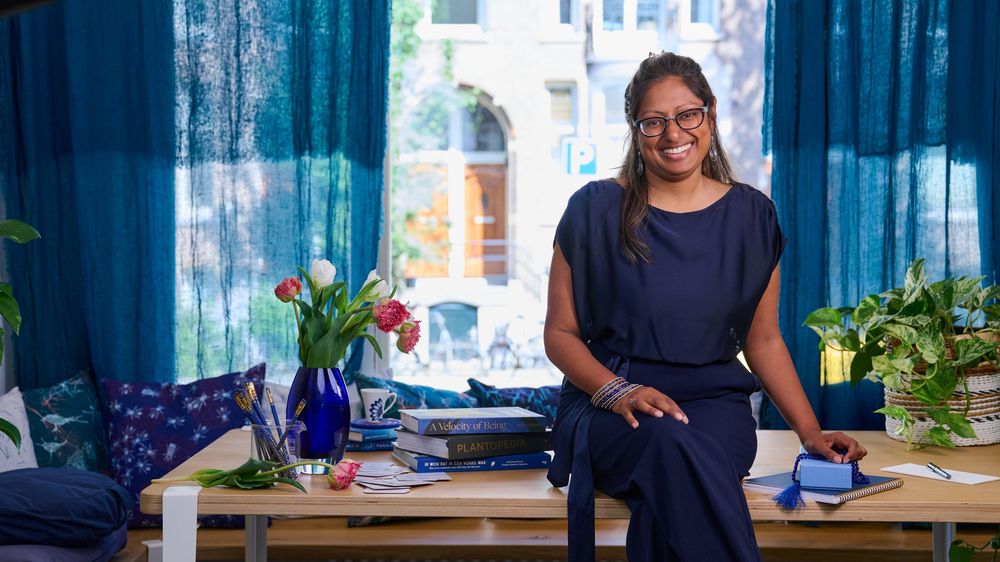 A person in a navy top sits at a desk decorated with blue curtains and colorful flowers.
