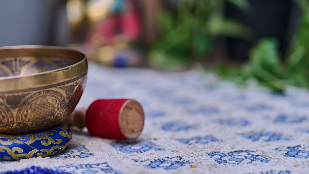 Copper Tibetan singing bowls and meditation instruments arranged on a blue and white patterned tablecloth.