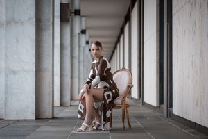 Someone sits elegantly in a pink vintage chair along a modern colonnade wearing ballet-inspired attire.